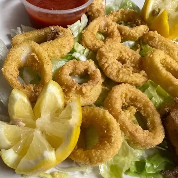 Golden fried calamari rings on a bed of lettuce with lemon wedges and a side of red sauce.