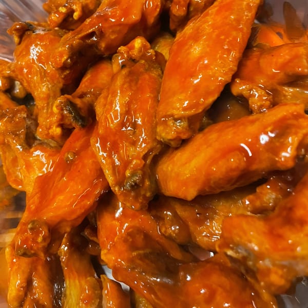 Close-up of JD's Pazzo Pizza's buffalo chicken wings, coated in shiny orange sauce.