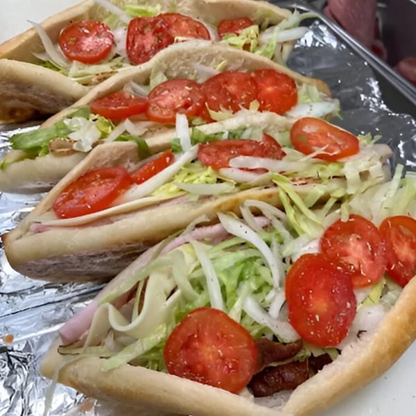 Four JD's Pazzo Pizza subs, filled with lettuce, onions, tomatoes, and meat, on foil.