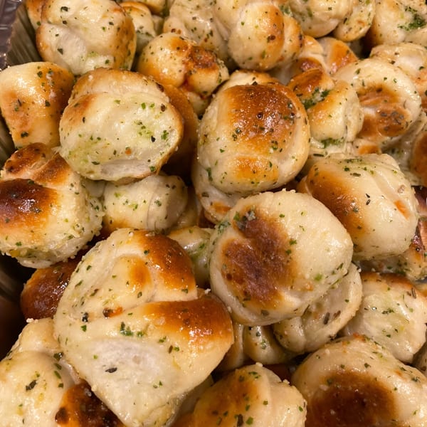 Close-up of golden-brown JD's Pazzo Pizza garlic knots, sprinkled with green herbs and glistening with oil.