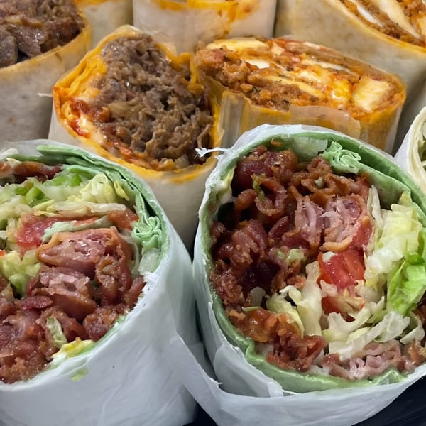 Close-up of several wraps, including two green tortilla wraps filled with bacon, lettuce, and tomato.