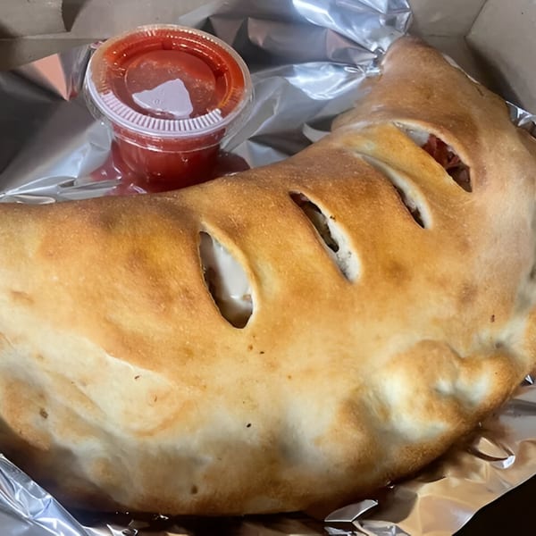 A golden-brown calzone with slits revealing melted cheese, served with a side of red sauce.