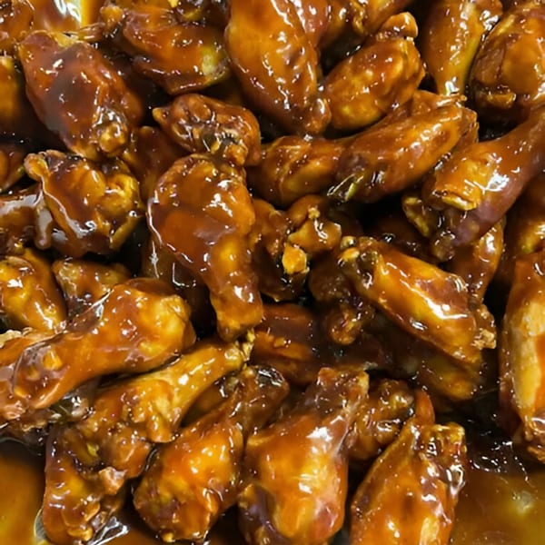 Close-up of numerous JD's Pazzo Pizza chicken wings coated in a glistening, sticky brown sauce.
