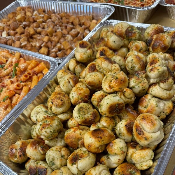 JD's Pazzo Pizza garlic knots, pasta, and potato cubes in catering trays.
